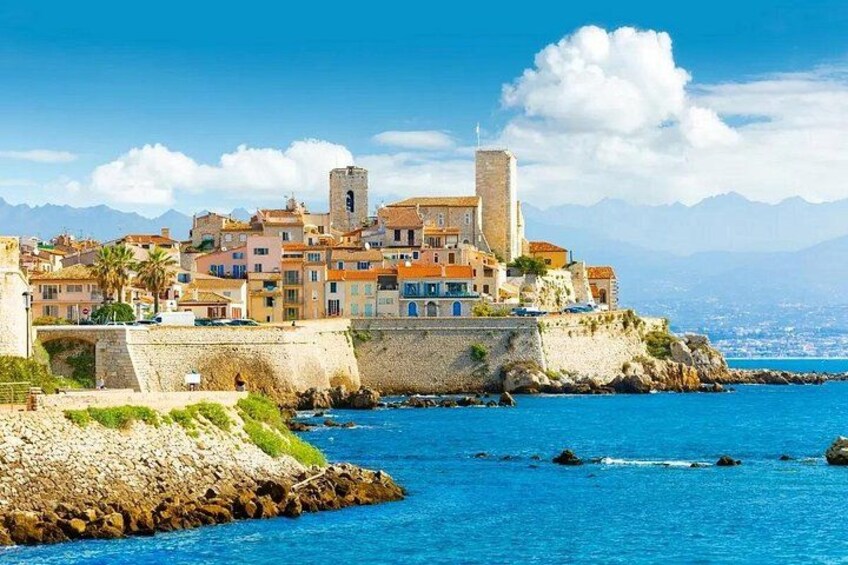 A coastal town with historic buildings, a prominent tower, and a clear blue sea. 1