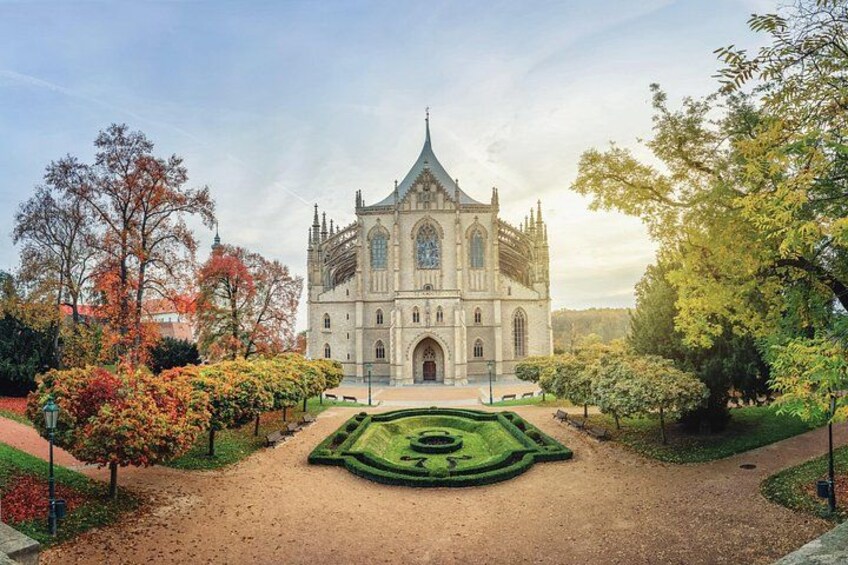 Une cathédrale historique à la façade symétrique, entourée d’un jardin à la française, avec des haies taillées et des arbres aux feuilles d’automne. 1