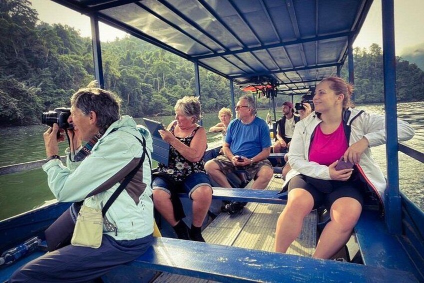 A group of people on a boat with a forested riverbank in the background. 2
