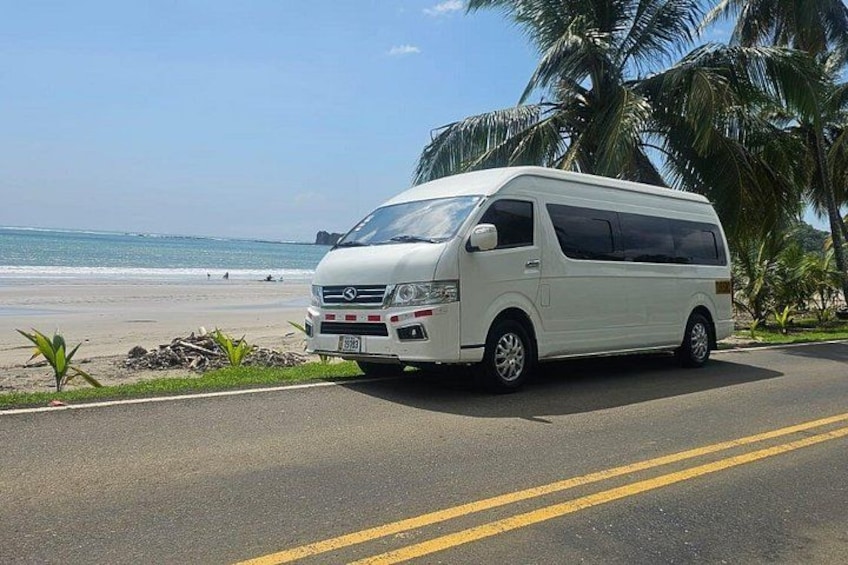 Una camioneta blanca estacionada en una carretera con una playa y palmeras al fondo. 5