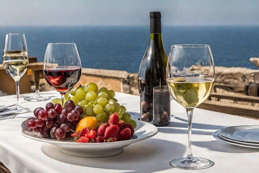 A table with a fruit platter, wine glasses, and a bottle of wine by a seaside view. 2