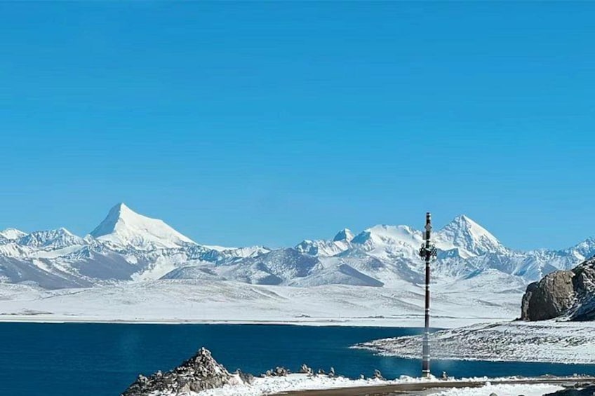 A snow-covered mountain range, a clear blue sky, and a body of water with a rocky outcrop in the foreground. 5
