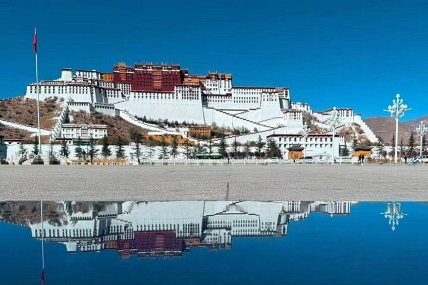A large, white, multi-tiered building with a red roof, reflecting in a calm body of water. 3