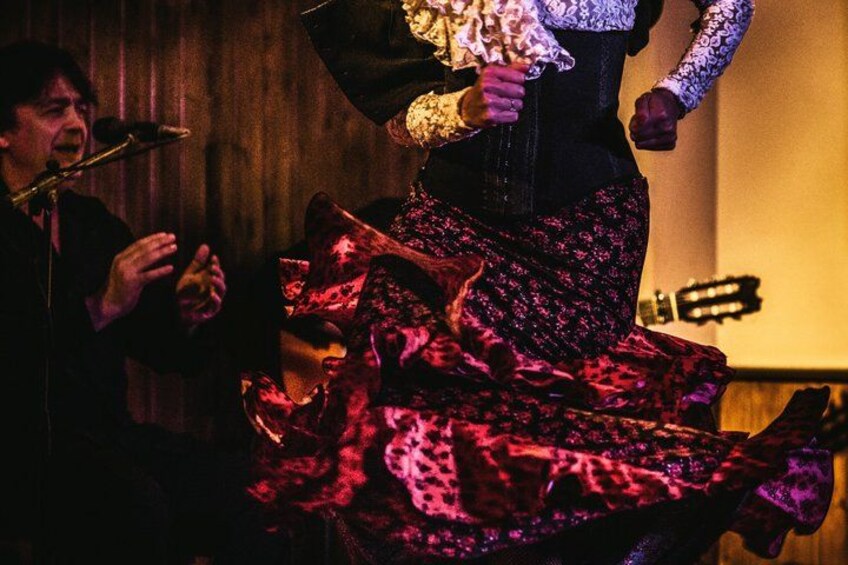 A person in a red patterned dress holding a bouquet, standing in a dimly lit room with a guitar in the background. 2