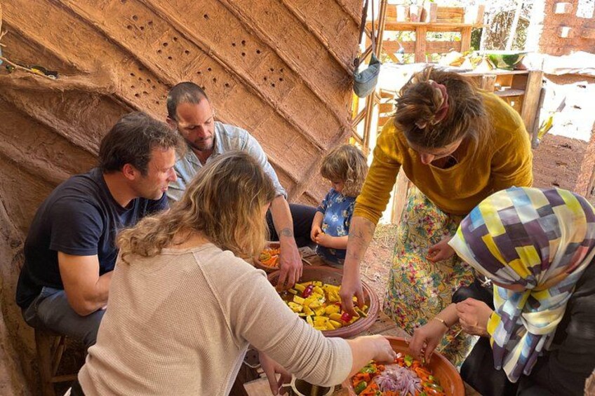A group of people engaged in a food preparation activity outdoors, with a rustic stone wall in the background. 5