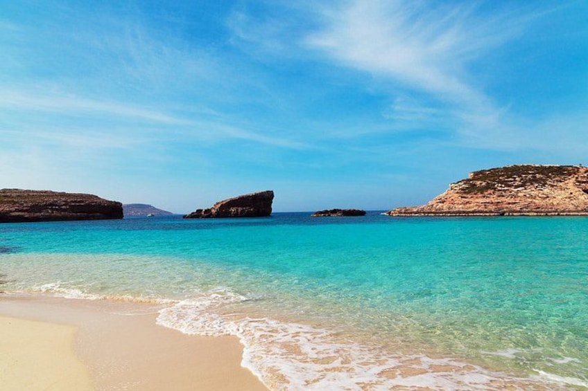 A beach with clear turquoise water, sandy shore, and rocky outcrops. 2