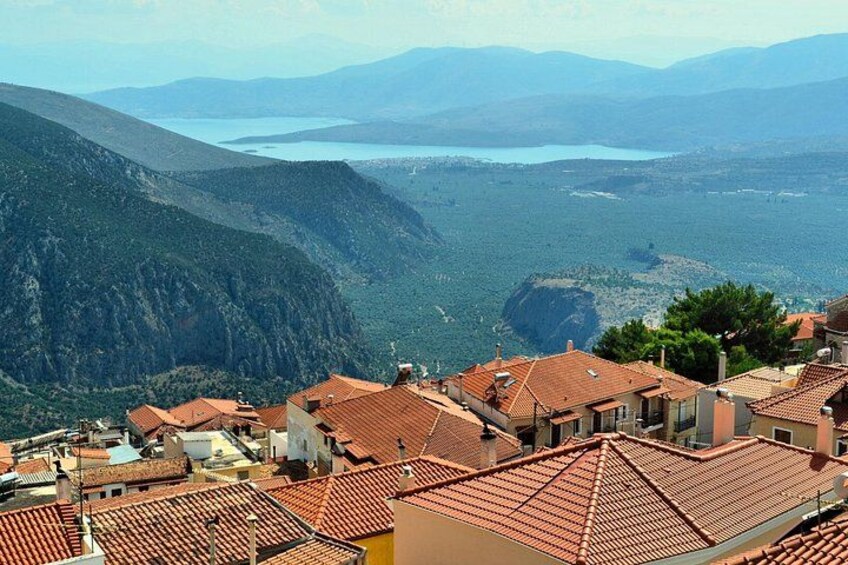 A coastal town with terracotta-roofed buildings, a mountainous backdrop, and a body of water in the distance. 3