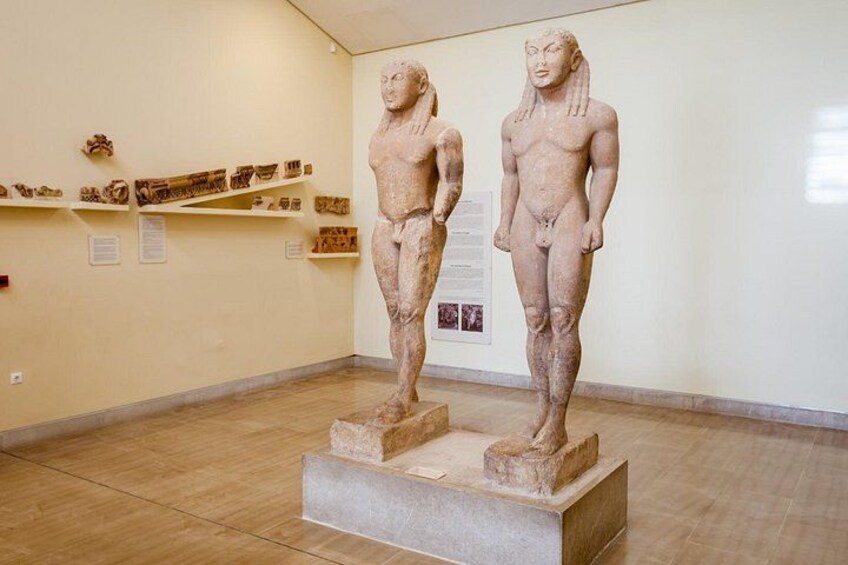 A museum interior with two ancient statues on pedestals, surrounded by informational displays. 5