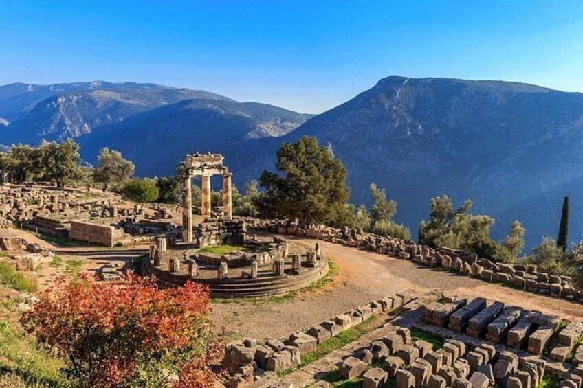 Ancient ruins with columns and stone structures, set against a mountainous backdrop. 1