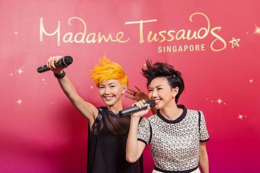 Dos personas sosteniendo micrófonos frente a un fondo rojo con el texto 'Madame Tussauds Singapore'. 4