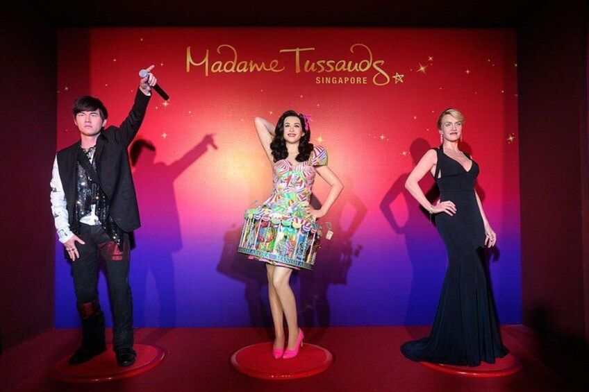 Tres personas en un escenario con un fondo que dice 'Madame Tussauds Singapore'. 2