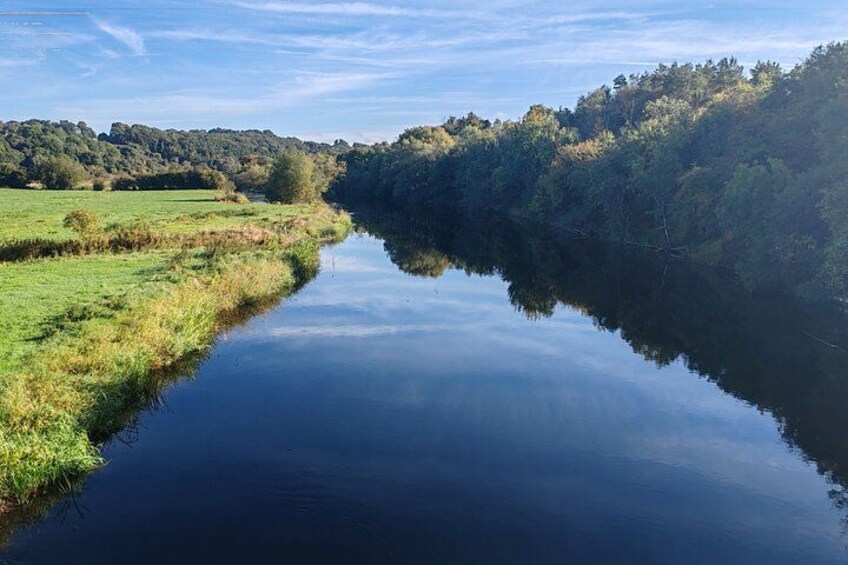 A calm river reflecting the surrounding trees and a clear sky. 2