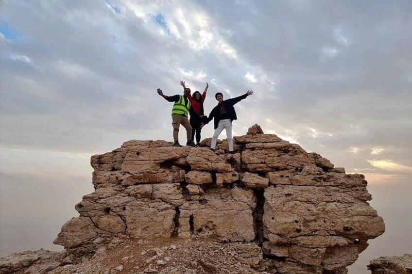 Three people standing on a rocky outcrop with their arms raised against a cloudy sky. 4