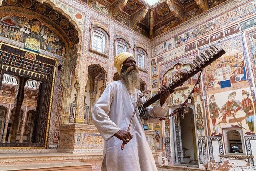 Ein Mann spielt ein traditionelles Saiteninstrument in einem prunkvollen Gebäude mit aufwendiger Kunst und Architektur. 1