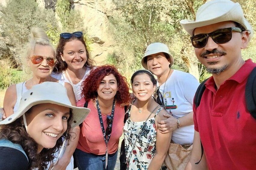A group of people outdoors, some wearing hats, with trees and rocky terrain in the background. 5