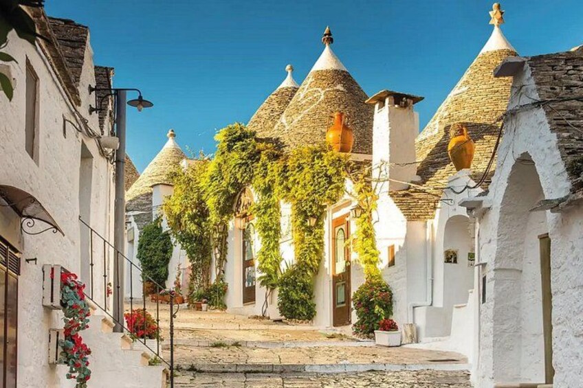 A cobblestone street with white buildings, conical roofs, and ivy-covered walls. 2