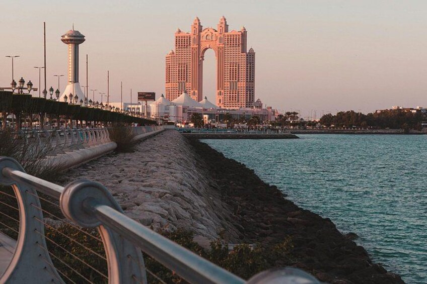 Une promenade en bord de mer, avec un grand hôtel, une tour et une mer calme. 5