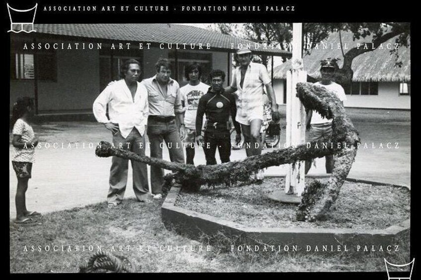 A sculpture of a large anchor in a garden with people standing around it. 4