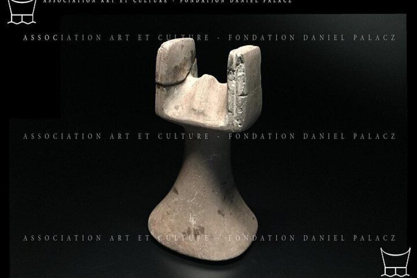 A sculpture of a human figure with a rounded head and a wide base, set against a dark background. 5