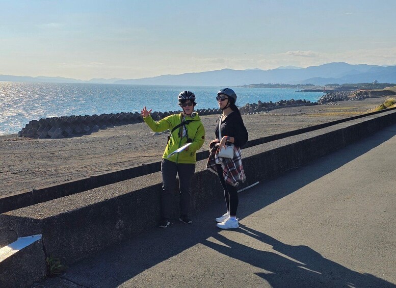 Two people standing on a coastal road with a view of the sea and mountains in the background. 1