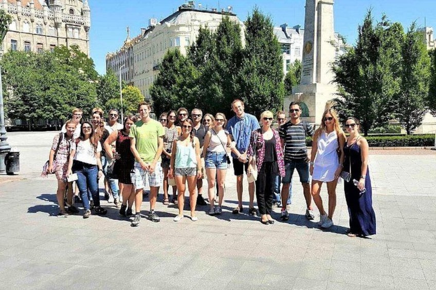 A group of people standing in a public square with buildings and trees in the background. 3