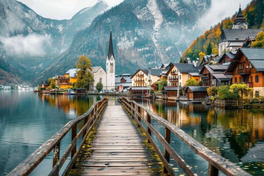 A wooden pier leading to a town with traditional buildings and a church, surrounded by mountains and a calm lake. 3