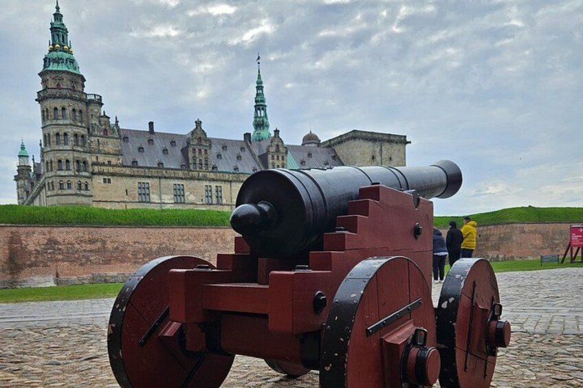 A cannon in front of a historic building with green spires. 3