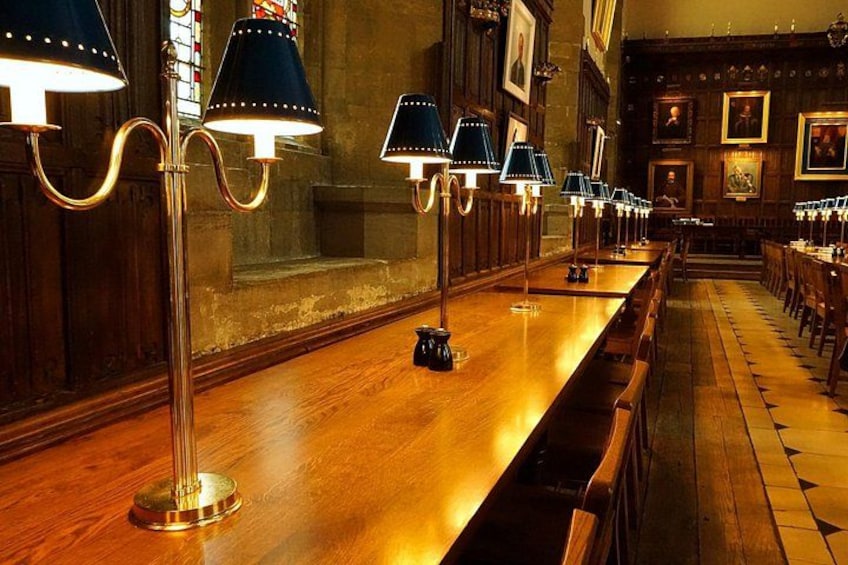 A long wooden table with lamps, framed portraits, and wooden benches in a room with stone walls. 5