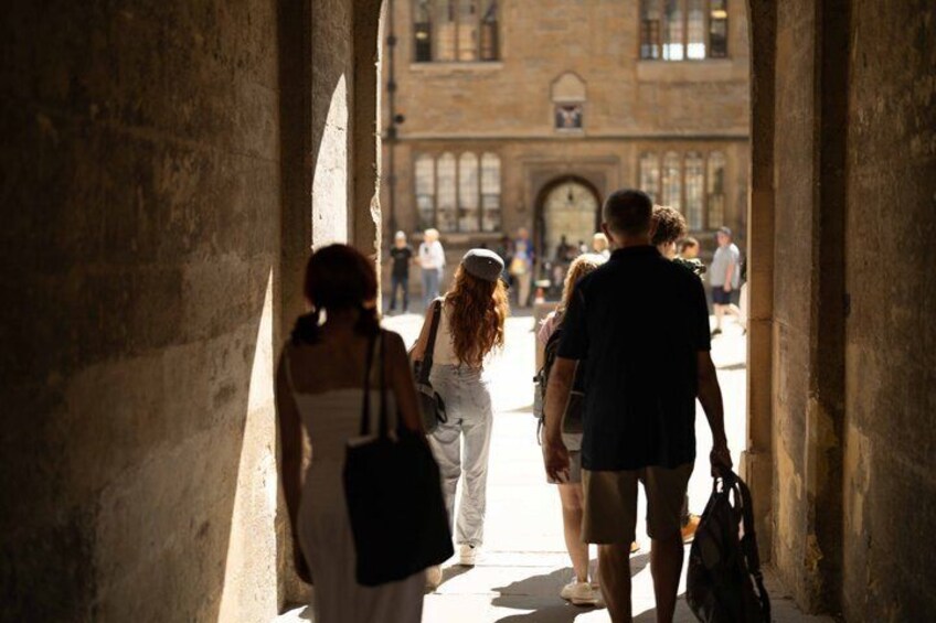 A group of people walking through a stone archway towards a historic building. 1