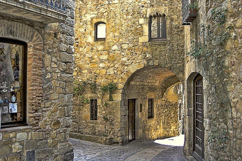 A stone building with arched doorways and windows, a cobblestone street, and a small balcony. 4