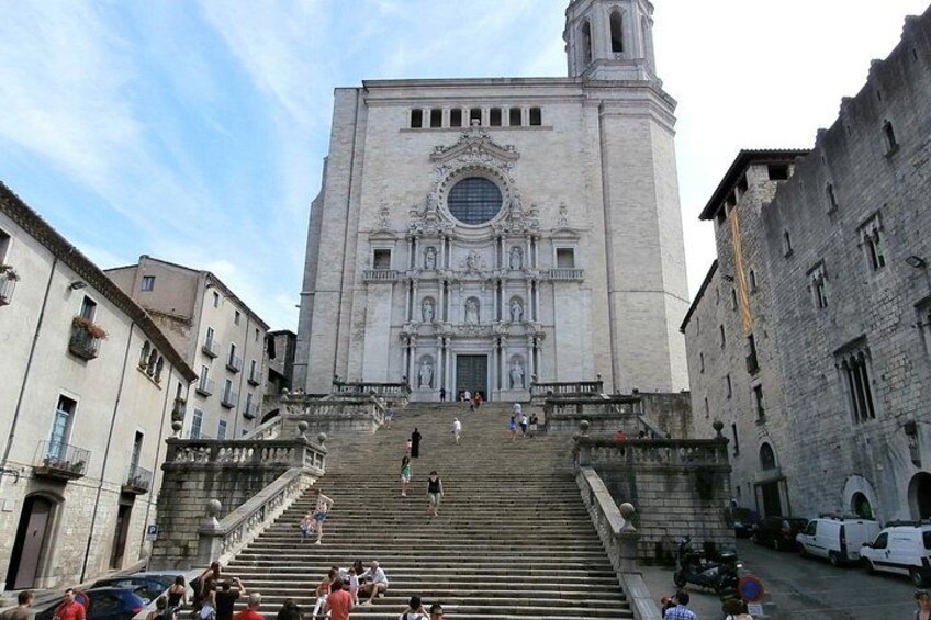 A grand cathedral with a bell tower, a staircase leading up to the entrance, and a busy street in the foreground. 5
