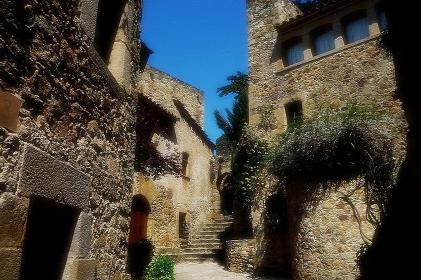 A narrow stone alleyway with buildings on either side, a wooden door, and a staircase leading up to a higher level. 3