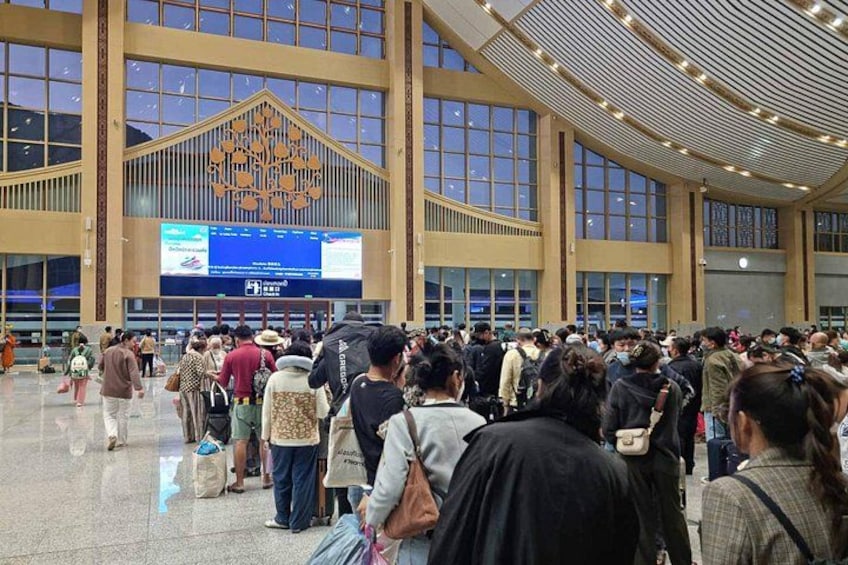 A crowded indoor space with large windows and a digital display screen. 3