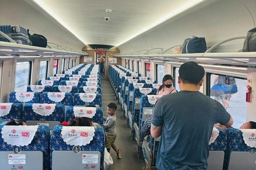 A train interior with rows of seats, passengers, and overhead luggage racks. 4
