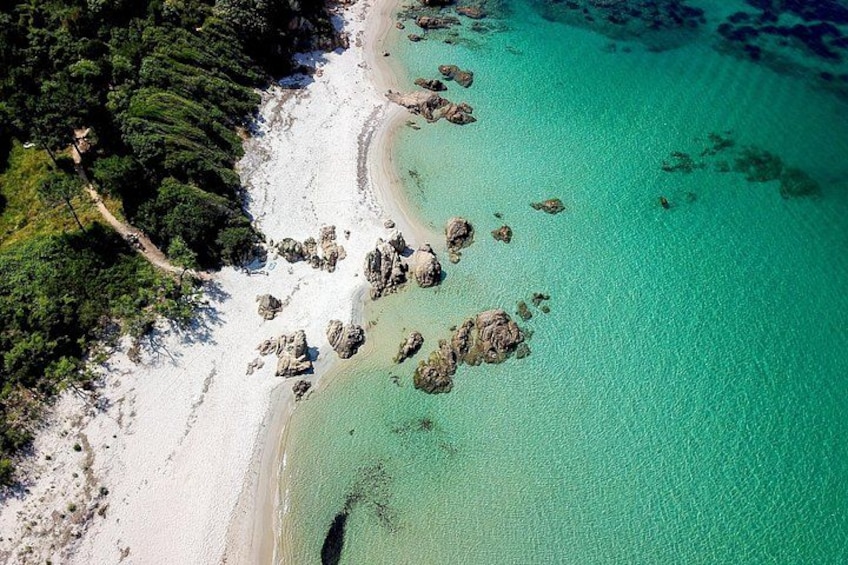 A coastal landscape with a sandy beach, clear turquoise waters, and scattered rocks. 3