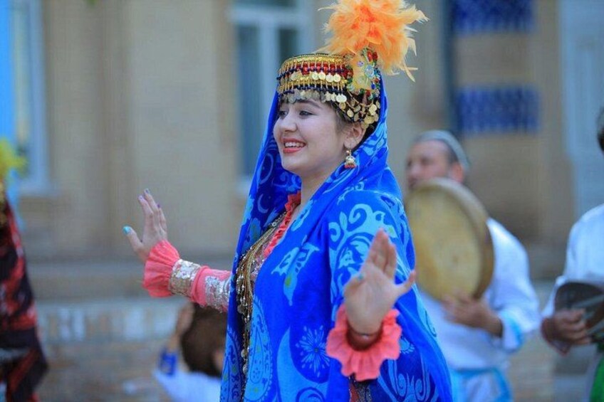 A person in traditional attire with a blue garment and a decorative headdress with orange feathers. 1