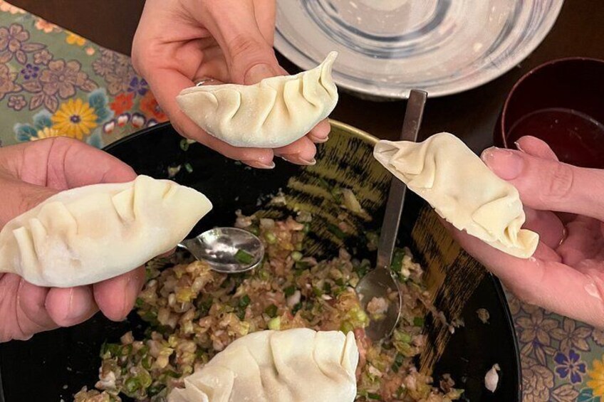 Manos sosteniendo dumplings sobre una sartén de comida. 5