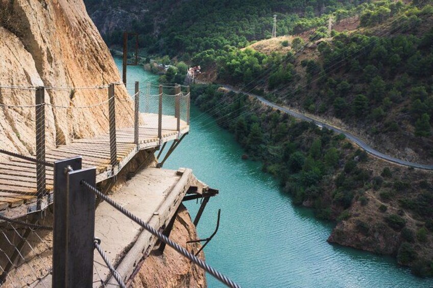 A wooden viewing platform overlooking a turquoise river, surrounded by lush greenery and a winding road. 4