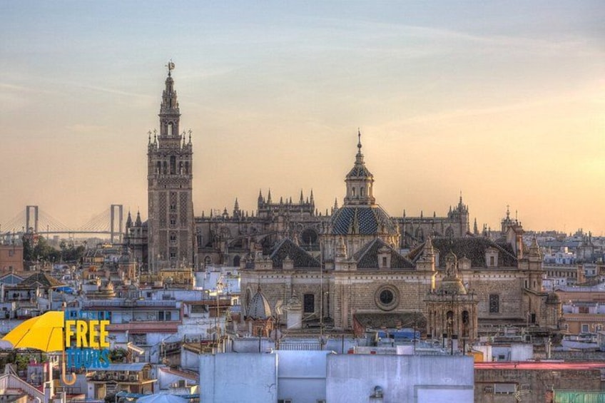 Un paisaje urbano histórico con una catedral destacada, una alta torre campanario y un puente al fondo. 5
