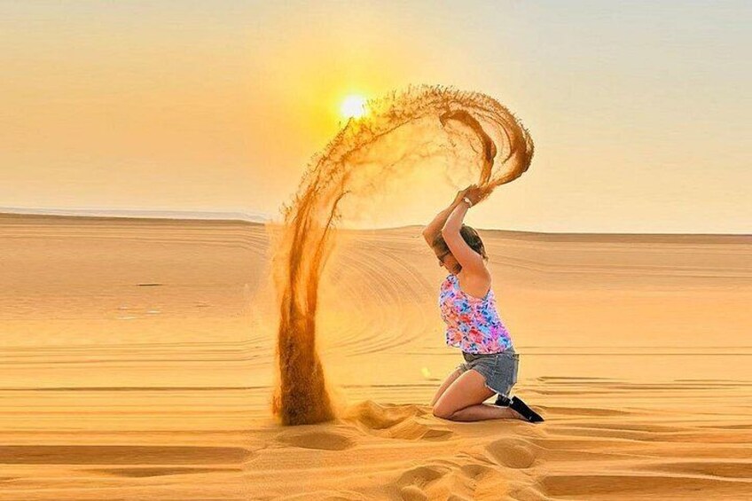 A person in a floral top and denim shorts performing a sand trick in a desert. 3