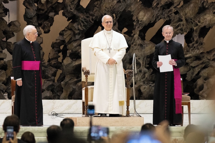 Three individuals in religious attire standing on a stage with a microphone stand and a book. 3