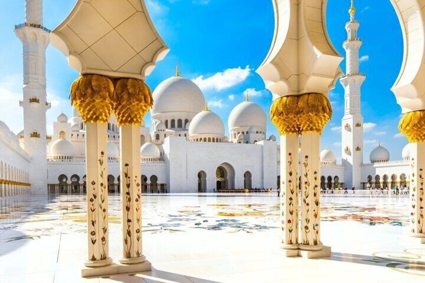 A white mosque with golden domes and columns, a large open courtyard, and a clear blue sky. 1