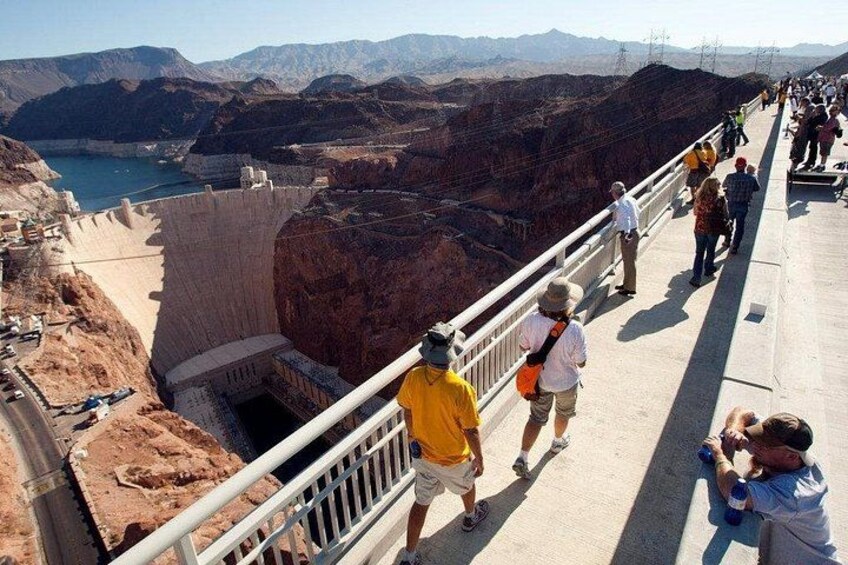 Een dam met een looppad, mensen wandelen, en een canyonlandschap. 1