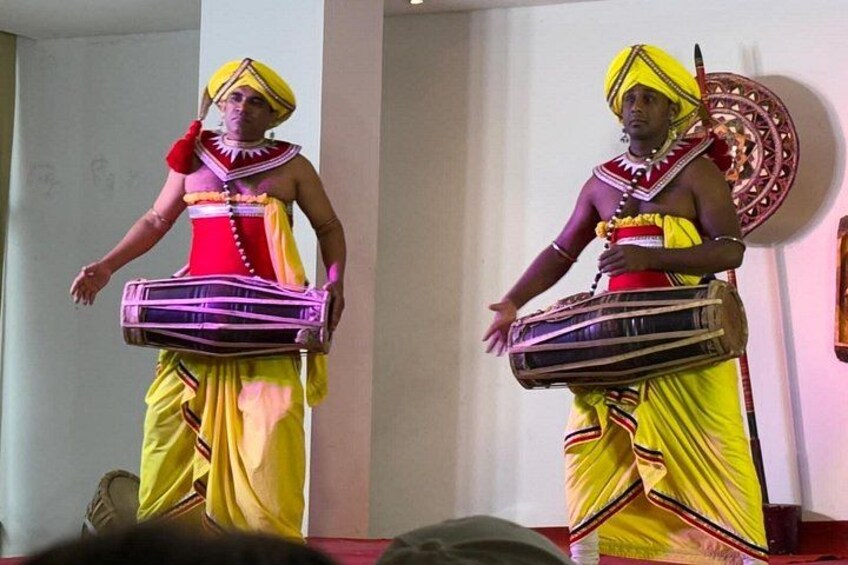 Two individuals in traditional attire with musical instruments, standing in an indoor setting. 5