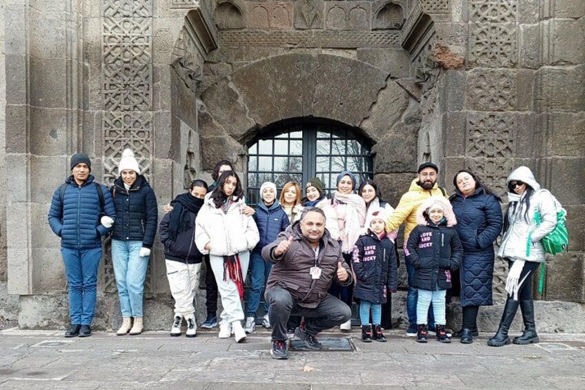A group of people standing in front of a stone building with intricate carvings and a large arched window. 2