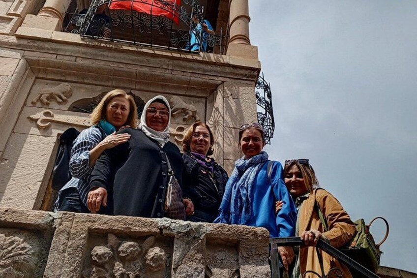 A group of people standing on a stone balustrade with ornate carvings, overlooking a building with a balcony. 5