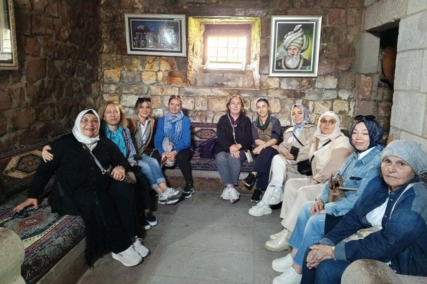 A group of people seated in a room with stone walls and a patterned carpet. 3
