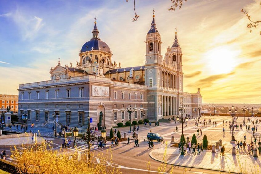 A large historic building with a dome and bell towers, surrounded by a plaza with people and trees. 3