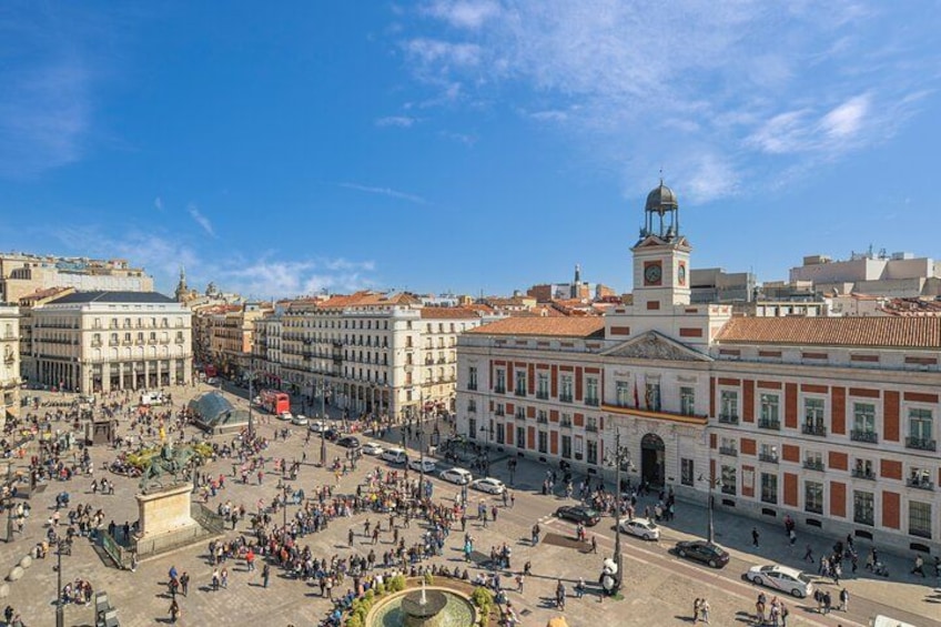 A bustling square with historic buildings, a prominent clock tower, and a fountain. 5