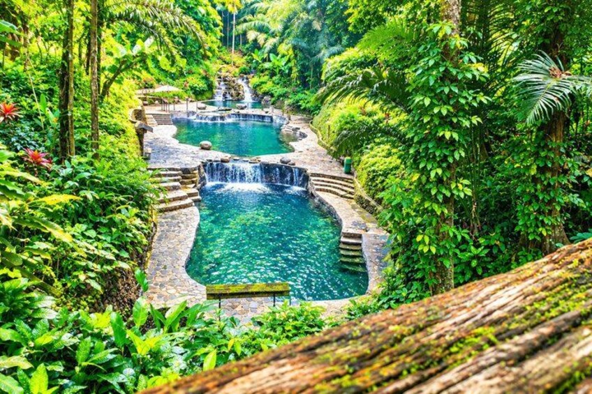 A natural pool with waterfalls surrounded by lush greenery. 1